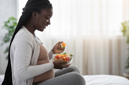 Pregnant woman on a bed eating a salad in an article about herbs to avoid during pregnancy 