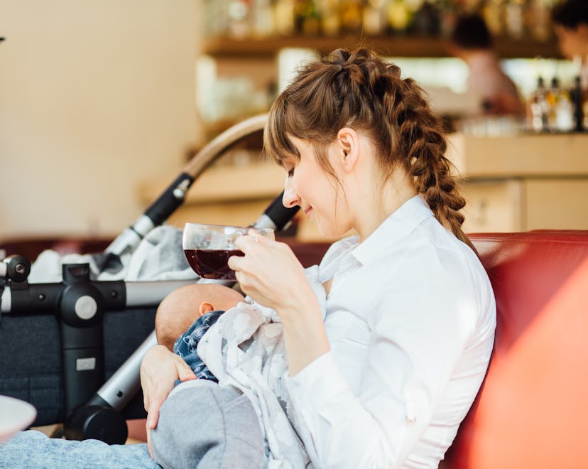 Attractive charming mother breastfeeding newborn son and drinking tea in cafe or restaurant.