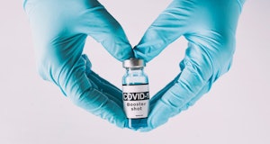 The shape of heart made from hands in gloves holding the covid vaccine booster shot