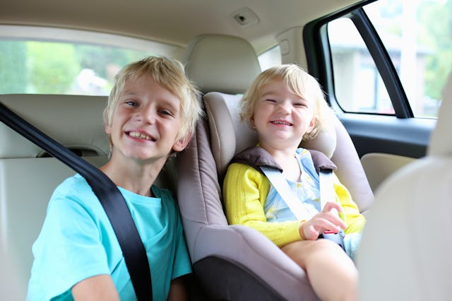 Happy kids, adorable toddler girl with teenager brother sitting together in modern car locked with s...