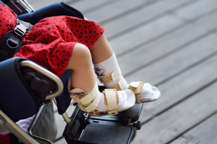 Child with AFO braces on both legs sits in wheelchair outside.