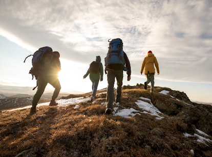 Group of four hikers with backpacks walks in mountains at sunset