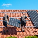 Two men installing new solar panels on the roof of a red-roofed house