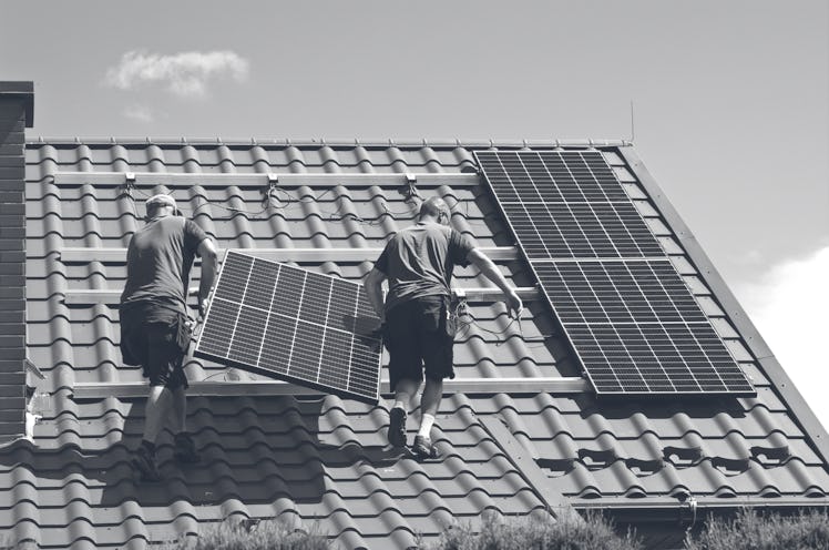 Two men installing new solar panels on the roof of a red-roofed house