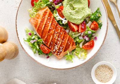 Grilled salmon fish fillet and fresh green lettuce vegetable tomato salad with avocado guacamole. To...