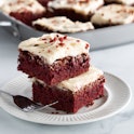 Two red velvet squares in a stack on a plate with other squares in soft focus in behind and copy spa...