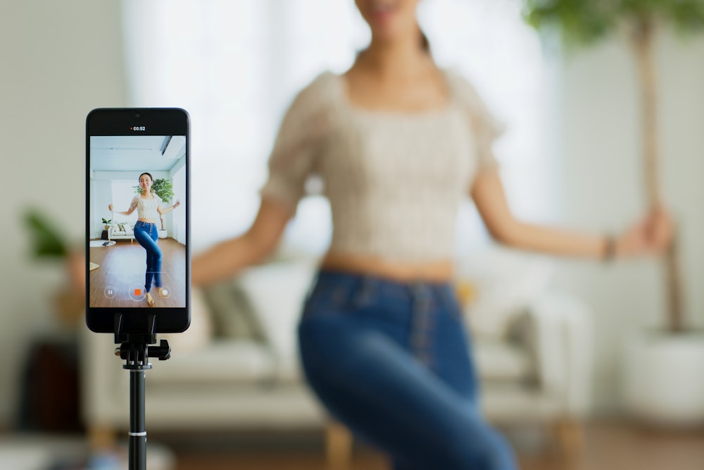 Asian young woman creates her dance video with smartphone camera.  To share a video to a social media app...