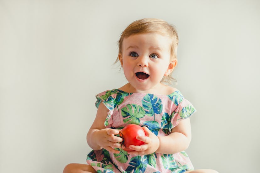 Baby girl surprised looking happy holding tomato in article about Virgo names for baby girls