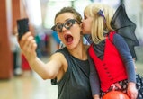 Trick or Treat. Portrait of trendy mother and daughter in bat costumes on Halloween at the mall taki...