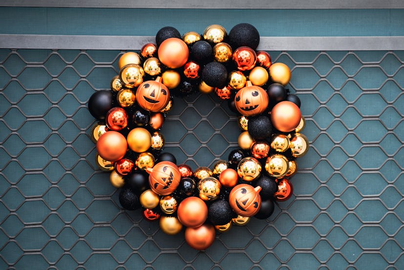Autumn wreath on the front door with orange and black pumpkins. Scenery for Halloween in October. De...
