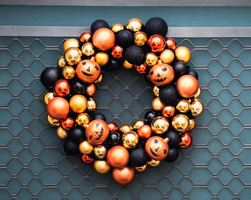 Autumn wreath on the front door with orange and black pumpkins. Scenery for Halloween in October. De...