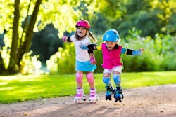 Girl and boy learn to roller skate in summer park. Children wearing protection pads and safety helme...