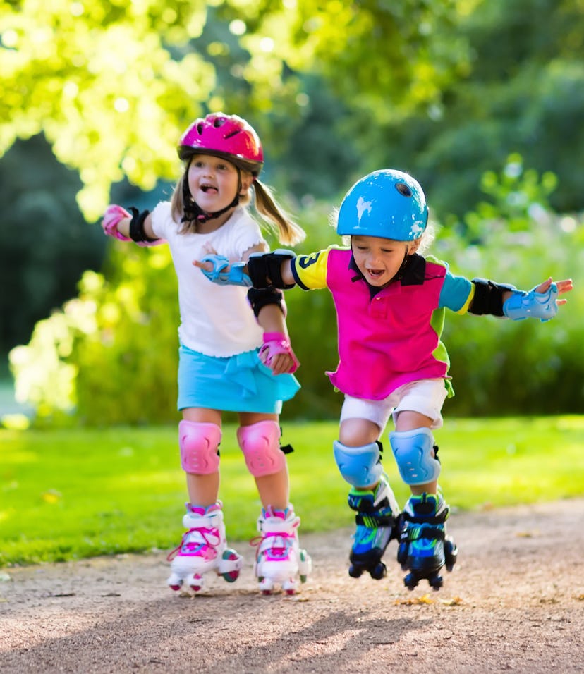 Girl and boy learn to roller skate in summer park. Children wearing protection pads and safety helme...