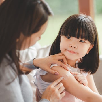 Mother helping her daughter applying bandage on the wound on shoulder at home 