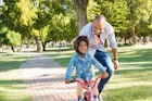 可爱的父亲教儿子在公园骑自行车。父亲帮助快乐兴奋的儿子骑自行车……