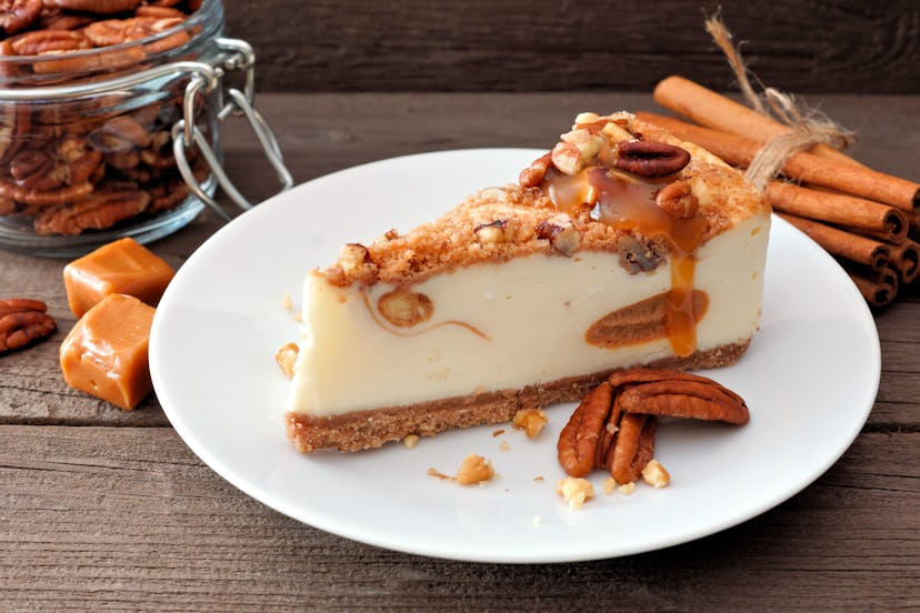 Slice of pecan caramel cheesecake on plate with a rustic wood background