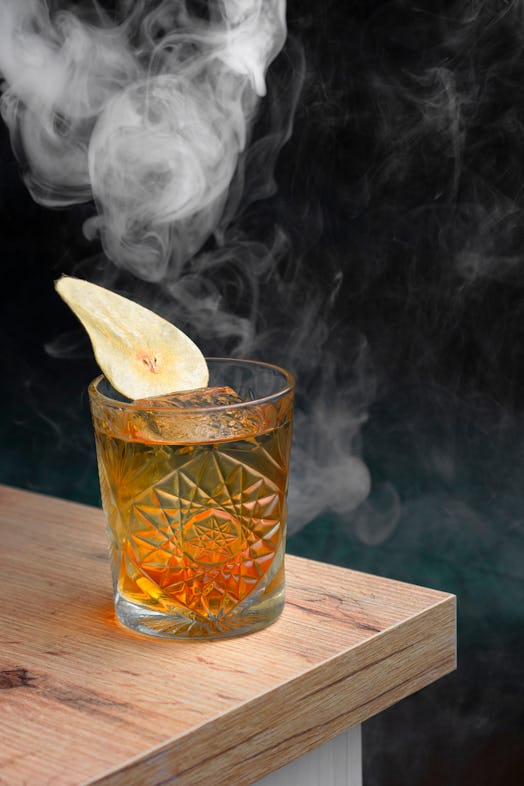 Close-up of amber cocktail with dried pear garnish in a lounge bar with smoke background