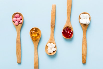 Vitamin capsules in a spoon on a colored background. Pills served as a healthy meal. Red soft gel vi...