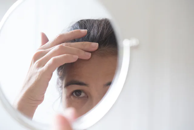 woman looks at her wrinkles in the mirror