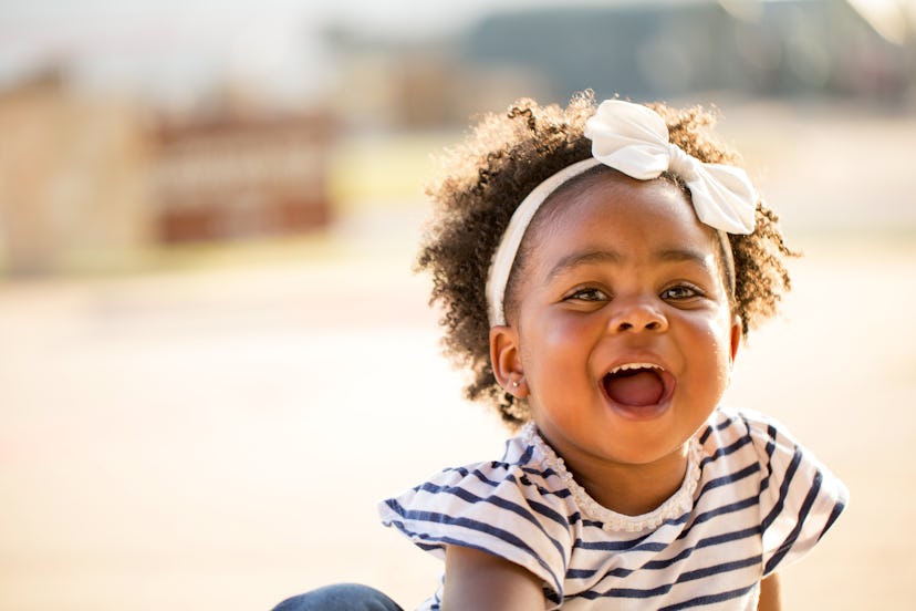 Happy African American little girl laughing and smiling outside in a round up of baby girl names tha...