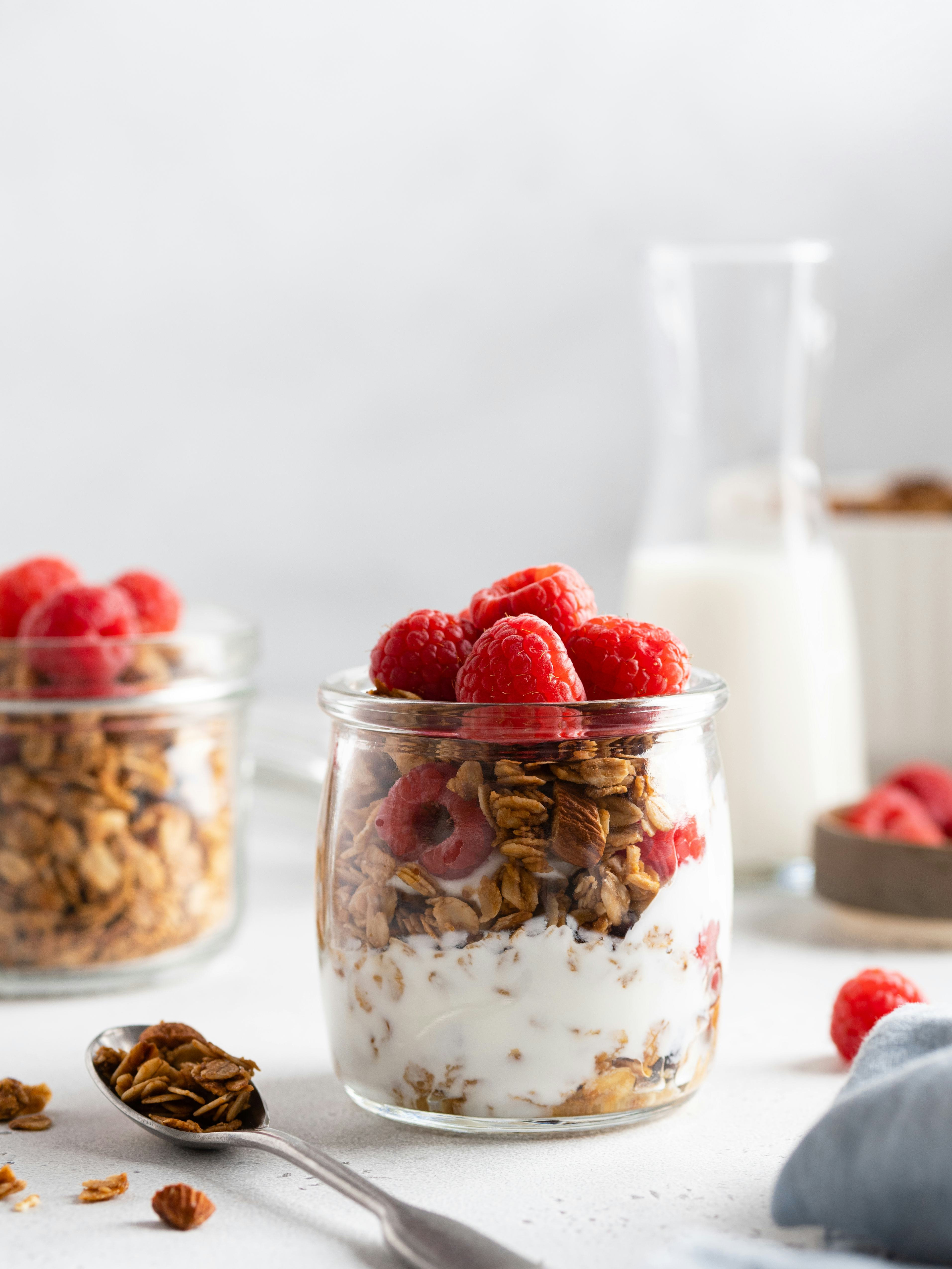 Granola (oatmeal muesli) with yoghurt in glass served with fresh raspberry, honey and milk. Tasty ve...