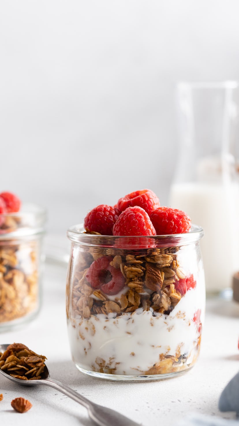 Granola (oatmeal muesli) with yoghurt in glass served with fresh raspberry, honey and milk. Tasty ve...