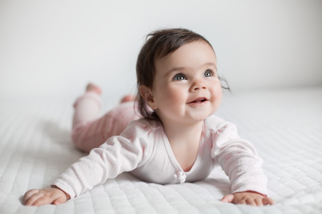 cute baby lies on stomach in bed on a white blanket in an article about girl names that start with D