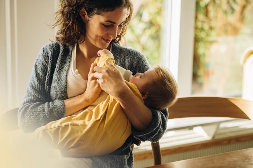 Mother feeding milk from bottle to her baby at home. Baby drinking milk from bottle.