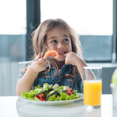 Portrait of cheerful asian girl eating salad with joy. She is looking aside with curiosity and smiling