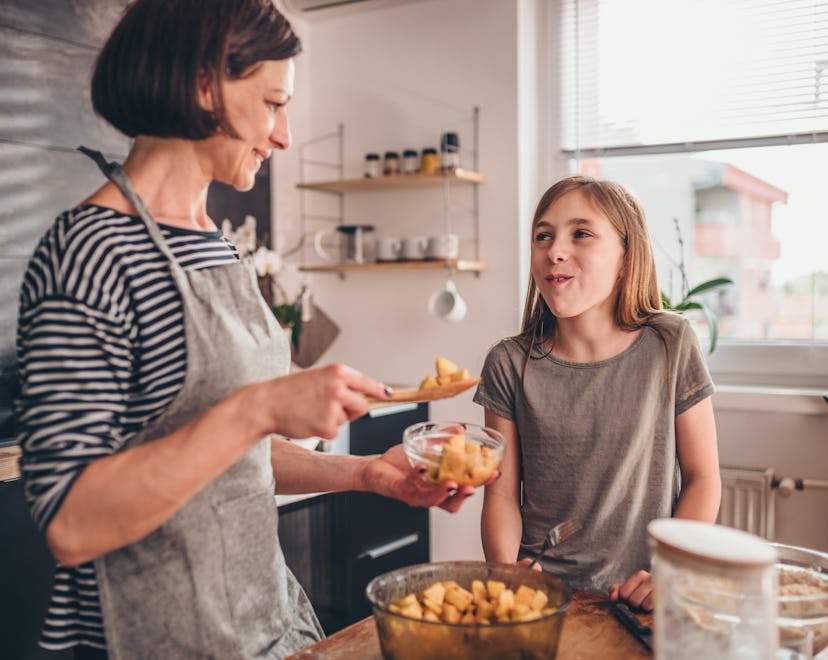 Mother and daughter tasting apple pie filling in the kitchen and finding more apple recipes to make.