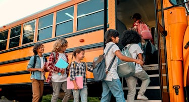 Back to school. Multiracial pupils of primary school near school bus. Happy children ready to study.