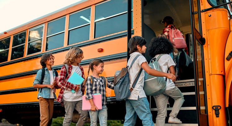 Back to school. Multiracial pupils of primary school near school bus. Happy children ready to study.