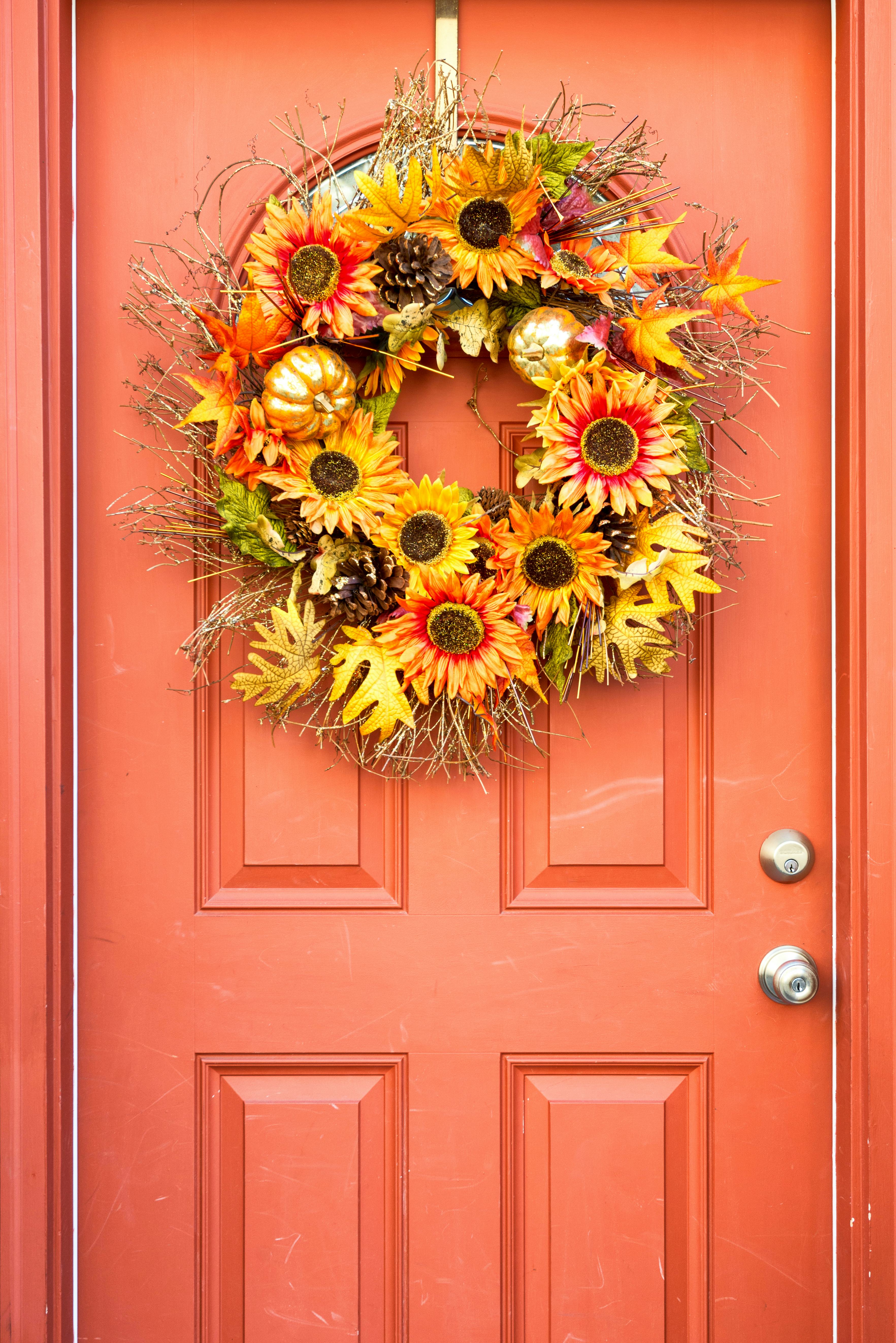 A fall wreath with orange and yellow flowers, golden pumpkins, leaves, and pinecones hanging on an o...