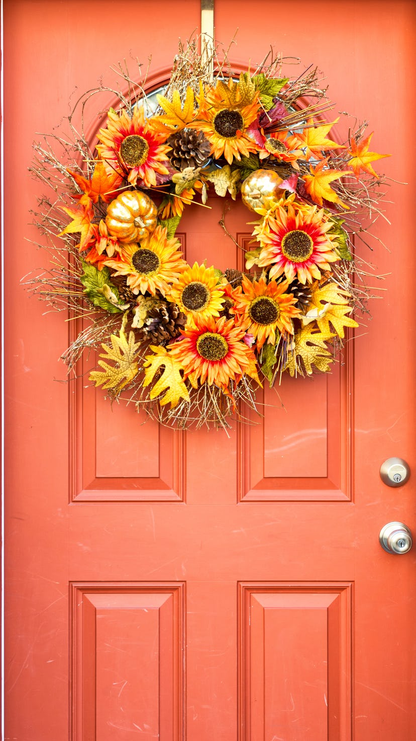 A fall wreath with orange and yellow flowers, golden pumpkins, leaves, and pinecones hanging on an o...