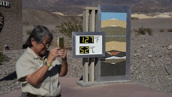 People visit a thermometer at the Furnace Creek Visitor Center, in Death Valley National Park, Calif...