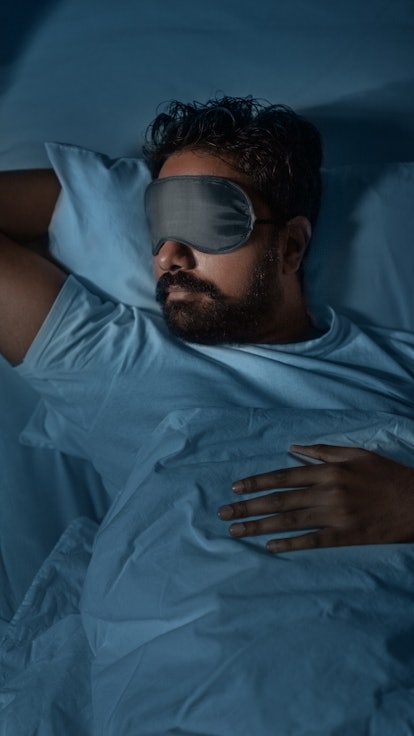 people, bedtime and rest concept - indian man in eye mask sleeping in bed at home at night