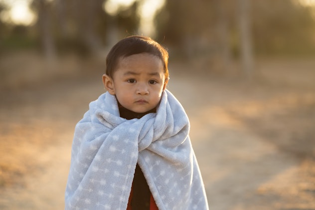 A child walks with a blanket wrapped around their shoulders like a cape. Quest is a Q name for boys.