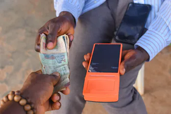 Hands of two african individuals doing financial transaction with a point of sales POS terminal as C...