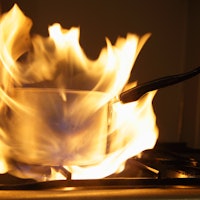 Old saucepan on fire on kitchen gas stove hob with orange big flame flash close up, indoor cooking f...