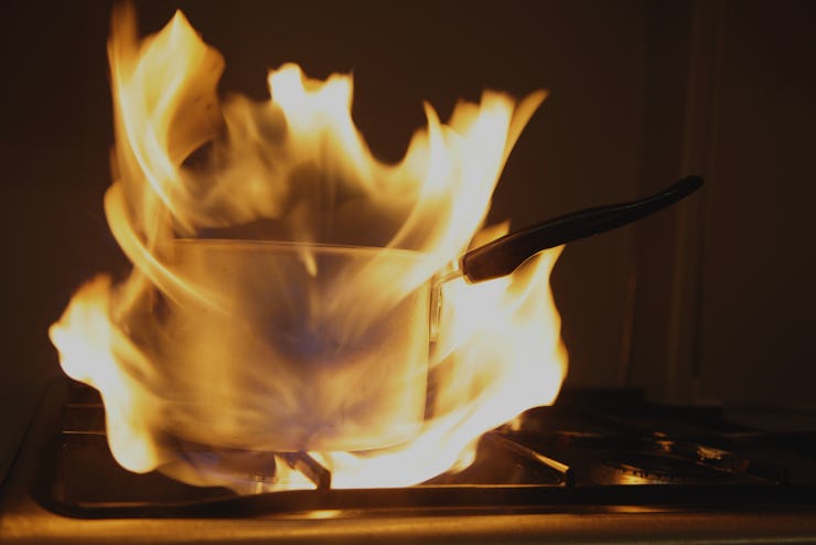 Old saucepan on fire on kitchen gas stove hob with orange big flame flash close up, indoor cooking f...