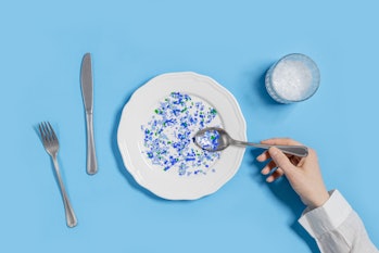 Plate with plastic pieces instead of food and glass of microplastics instead of water. Microplastic ...