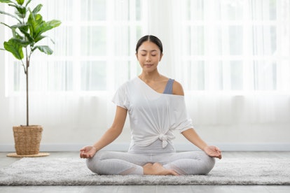 Wellness asian young woman sit on carpet breathing in tranquility yoga lotus pose, y yoga meditation.