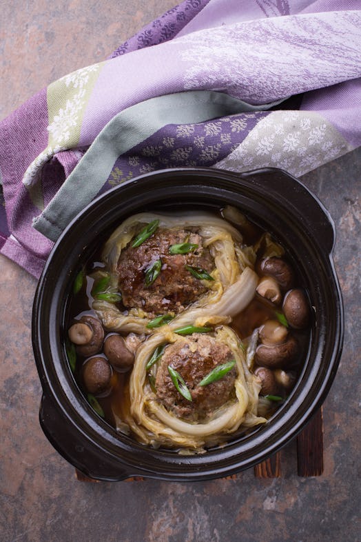 Lion's head meatballs with Napa cabbage served in a black claypot. Stone background , purple dishtow...