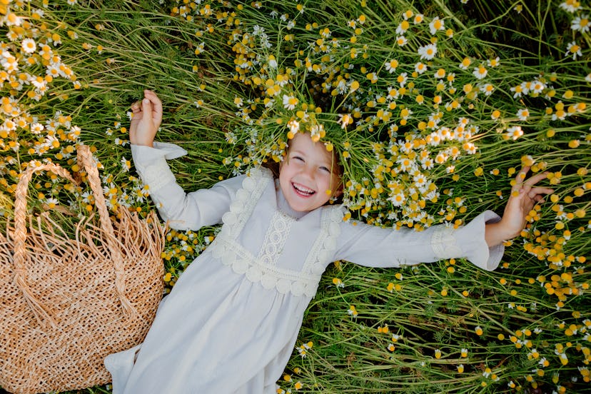 A girl lies down smiling in a field of flowers. Vale is a unique girls name that begins with V.