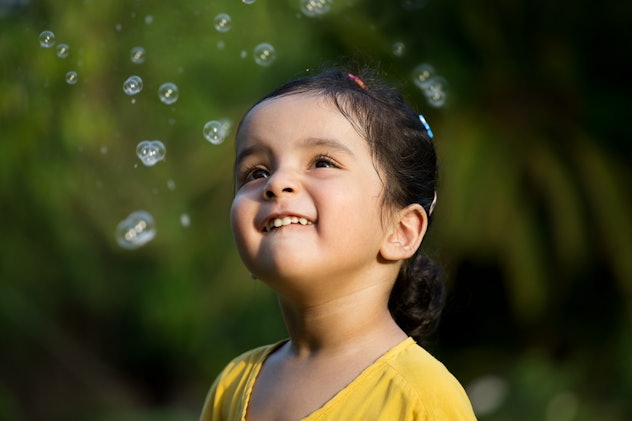 A little girl smiles looking at bubbles. Veda is a beautiful girl name that begins with V.