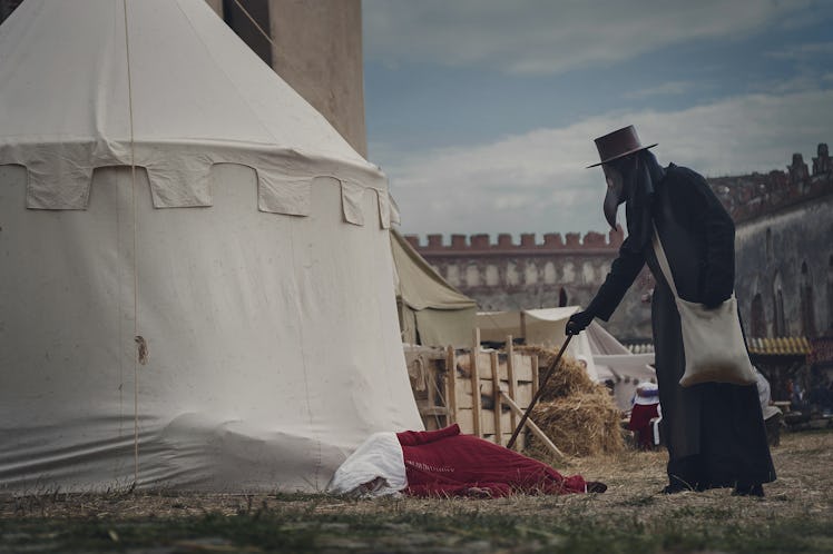 A masquerade historical scene reconstruction. Plague doctor in medieval old town touch a fallen woma...