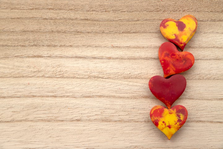 Four red and yellow Melted Wax crayon hearts in a row on a wood grain background with copy space