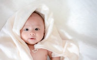 Adorable, Asian newborn laying with white blanket in article about boy names that begin with Y