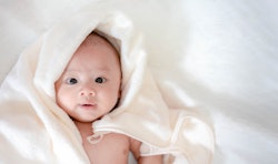 Adorable, Asian newborn laying with white blanket in article about boy names that begin with Y