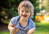 Portrait of Cute baby boy with Down syndrome playing in summer day on nature in article about spring...